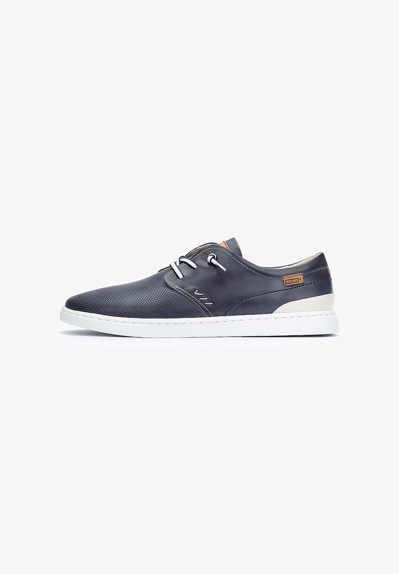 Chaussures décontractées bleu foncé avec texture perforée, semelle blanche, lacets gris et un accent beige sur le côté. Caractérisées par un design lisse et une silhouette basse.