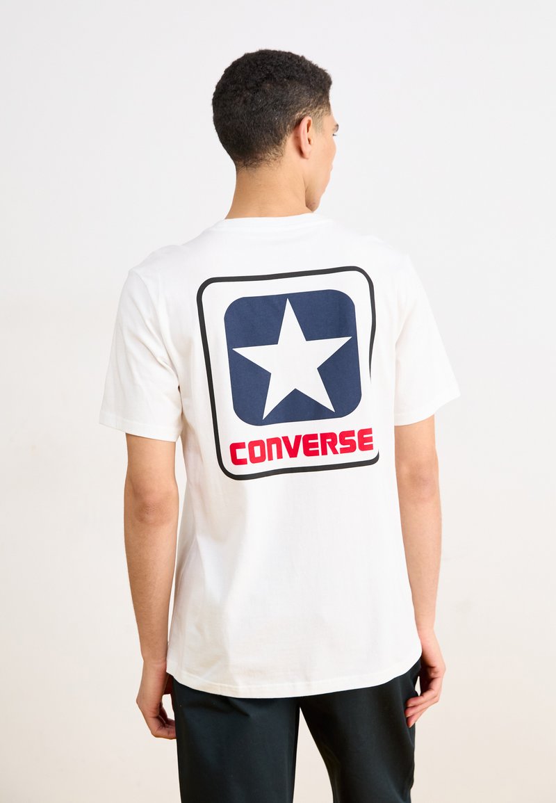 Camiseta de algodón blanca con un gran gráfico de estrella en color marino bordeado en negro y la palabra "CONVERSE" en rojo en la parte de atrás. Mangas cortas.
