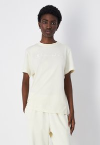 Light yellow cotton t-shirt with short sleeves and a crew neck, featuring embroidered "Champion" logo across the chest.