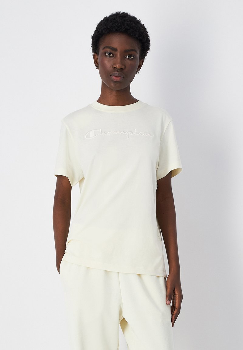 Light yellow cotton t-shirt with short sleeves and a crew neck, featuring embroidered "Champion" logo across the chest.