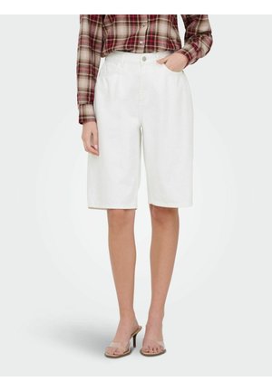 Persoon draagt witte shorts tot op de knie, een geruit overhemd met lange mouwen in de broek gestopt, en hoge hakken met doorzichtige bandjes.