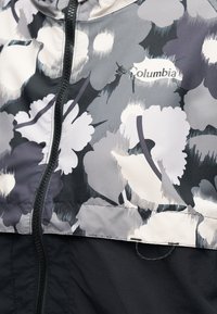 Μαύρο και γκρι μπουφάν Columbia με λουλουδάτο σχέδιο, φερμουάρ μπροστά και ορατό λογότυπο της εταιρείας στην περιοχή του στήθους.