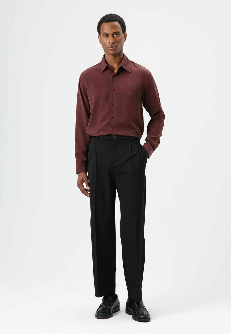 Chemise bordeaux à manches longues avec fermeture à boutons, associée à un pantalon noir taille haute et des chaussures noires ; textures lisses, coupe ajustée.