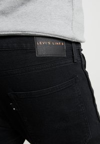 Jeans in denim nero con etichetta in pelle Levi's Line 8 sulla vita. Caratteristiche includono tasche posteriori e una texture liscia con dettagli di cucitura.