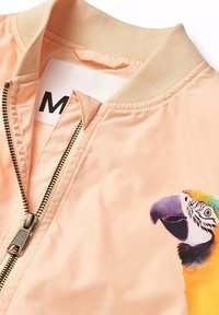 Persikofärgad bomberjacka med dragkedja. Har en färgglad papegoja grafisk design på bröstet samt ribbade kragar och muddar.