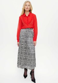 Rote, geraffte Bluse mit Knopfverschluss, kombiniert mit einem Maxirock im Schwarz-Weiß-Muster. Schwarze High Heels runden das Outfit ab.
