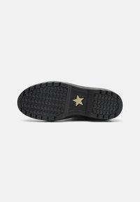 Suela de zapato de goma negra con un patrón de textura, que presenta un emblema dorado en forma de estrella en el centro. Diseño plano adecuado para varios tipos de calzado.