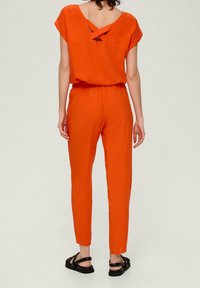 Orange jumpsuit med en løs pasform, korte ærmer og et krydset rygdesign. Fremstillet af et let stof med tapered bukser.