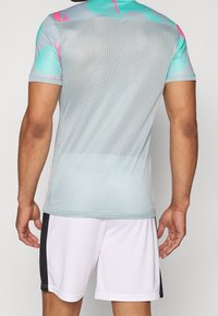 Lätt grå sporttröja med mesh-struktur, med livfulla turkosa och rosa detaljer på axlarna, i kombination med vita shorts.