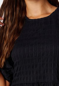 Haut noir texturé avec un motif froissé ; doté d'un col rond et de manches courtes, mettant en valeur un design froncé.