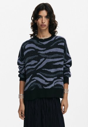Maglione a righe nere e lavanda con tessuto testurizzato, scollatura rotonda e maniche a sbuffo. Bracciale in argento al polso, indossato con una gonna nera.