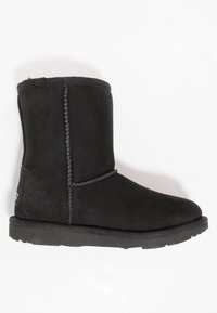 Bota de invierno negra de ante hasta la mitad de la pantorrilla con costuras visibles y suela plana de goma, mostrada sobre un fondo blanco.