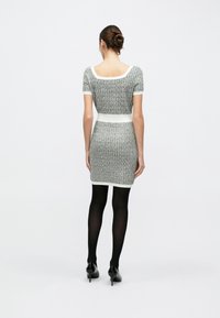 Φόρεμα bodycon με σχέδιο σε ύφασμα tweed σε μαύρο και άσπρο, κοντά μανίκια, εφαρμοστή σιλουέτα, αντιπαραβλημένο με λευκή ζώνη στη μέση, συνδυασμένο με μαύρα καλσόν και ψηλοτάκουνα.