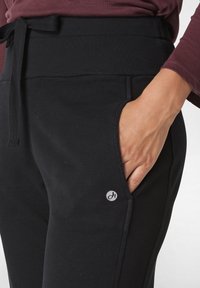 Zwarte sweatpants gemaakt van zachte stof met een elastische tailleband en een trekkoord. Beschikt over zijzakken en een klein logo op de onderbenen.