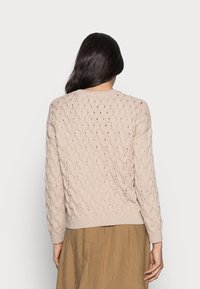 Béžový pletený svetr s texturovaným, otevřeným vzorem, dlouhými rukávy, žebrovanými manžetami a lemem. Zobrazen zezadu s hladkou látkou.