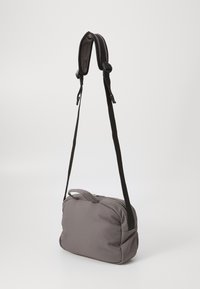 Borsa a tracolla grigia in tessuto con una forma strutturata, chiusura con zip e tracolla nera regolabile. Texture liscia con un piccolo manico superiore.