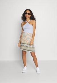 Top cropped azul claro com nervuras e alças cruzadas, combinado com uma saia mini de padrão floral com detalhes em verde, bege e branco. Ténis brancos.