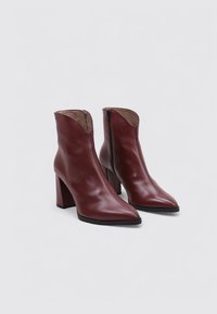 Botas de tobillo de cuero burdeos con punta afilada, cremallera lateral y tacón grueso. Textura suave con costuras decorativas en la parte superior.