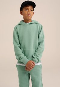 Felpa verde menta con tasca a marsupio, polsini a costine e morbida texture, abbinata a pantaloni coordinati e un cappellino nero.