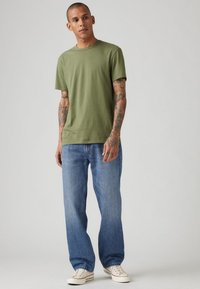 Oliven grøn bomulds t-shirt med rund hals, parret med lyseblå lige ben jeans og hvide snørresko.