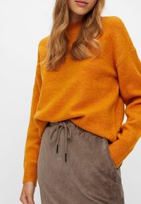 Orange stickad tröja med lös passform, ribbade ärmslut, i kombination med en brun corduroykjol med dragsko i midjan och vertikal ribbning.