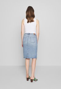 Světle modrá džínsová tužková sukně s zadními kapsami, s vertikálním švem a rozparkem na lemu, spárovaná se zelenými a hnědými sandály na vysokém podpatku.