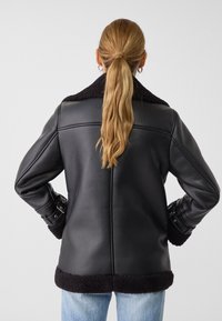 Veste en cuir noir avec un col et des poignets en shearling, présentant une coupe légèrement oversize et des détails de boucle sur les manches.