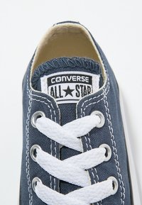 Sininen kangaskengät valkoisilla nauhoilla, hopeisilla rei'illä ja repaleisella reunalla. Sisältää logopatchin, jossa lukee "Converse All Star."