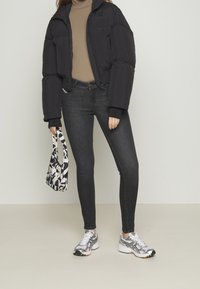 Chaqueta puffer negra, diseño corto, con un cuello de tortuga beige, jeans oscuros, zapatillas plateadas y un bolso de patrón blanco y negro.