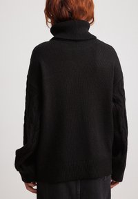 Svart stickad polotröja med avslappnad passform, med kabelstickade mönster på ärmarna och ribbade fållar och ärmslut.