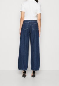 Vidbenade denimbyxor i mörkblått med hög midja. Funktioner inkluderar två bakfickor och en ren nederkant. Kombineras med en vit topp.