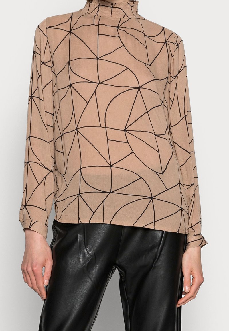 Blouse à manches longues en beige clair avec un motif géométrique noir, dotée d'un col montant froncé et d'un tissu doux et léger.