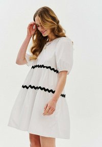Biele bavlnené šaty s nadýchanými rukávmi a čiernym volánikom. A-línie, po kolená, hladká textura, s okrúhlym výstrihom.