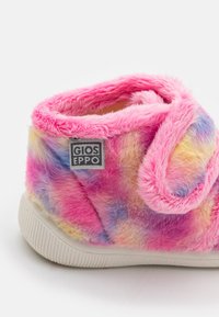 Lämmin vaaleanpunainen, violetti ja keltainen pörröinen tossu, jossa on valkoinen pohja, kankainen tarrasankka ja Gioseppo-brändin etiketti sivulla.