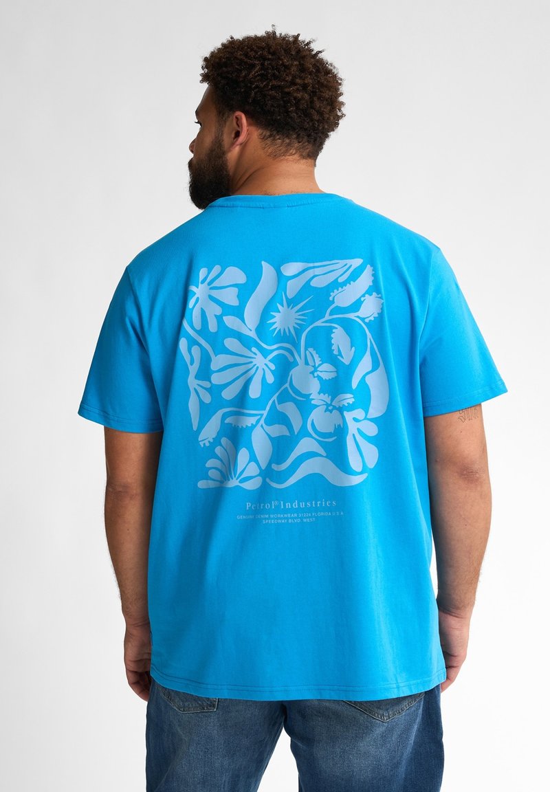 Modrá bavlněná tričko s velkým světle modrým grafickým designem na zadní straně, obsahující abstraktní tvary a rostliny. Volný střih, krátké rukávy.