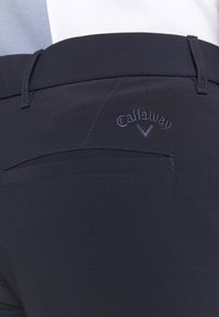 Navy golf pants made of smooth fabric with a subtle sheen, featuring a back pocket and embroidered Callaway logo above it.