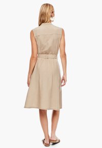 Ärm- och bälteslös beige klänning i linne-liknande tyg, knälång fåll och en enkel, strukturerad design.