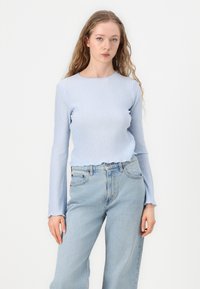 Light blue ribbed long-sleeve top with a scalloped hem, paired with light wash high-waisted jeans. Smooth texture and fitted design.