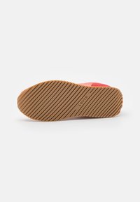 Baskets rouges avec une semelle en caoutchouc texturée, présentant un motif rayé et une semelle extérieure beige en contraste. Nom de la marque "Levi's" embossé sur le talon.