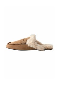 Mocassin en suède beige avec une douce doublure et bordure en fausse fourrure, présentant un détail de couture décoratif et un design à dos ouvert. Semelle plate noire.