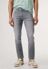 Vaqueros de denim gris con corte recto, que presentan cinco bolsillos y un ligero desgaste, combinados con una camiseta casual de rayas menta y zapatillas beige.