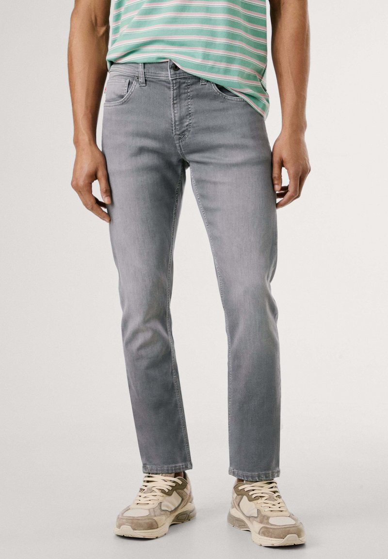 Vaqueros de denim gris con corte recto, que presentan cinco bolsillos y un ligero desgaste, combinados con una camiseta casual de rayas menta y zapatillas beige.
