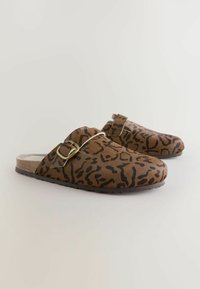 Sabots en imprimé léopard marron avec un dessus texturé doux, une sangle réglable et une boucle en ton doré. Semelle plate avec texture antidérapante.