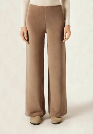 Pantalons large à côtes marron avec une texture douce, dotés d'une taille haute et d'un design fluide et lisse.