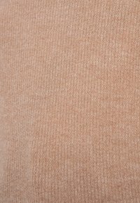 Tissu doux et tricoté de couleur pêche claire avec une texture côtelée. Les fibres visibles créent une apparence chaude et confortable. Pas de motifs ou accents distincts.