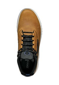 Zapatilla de cuero marrón con detalles en negro, parte superior texturizada, ojetes redondos para los cordones y suela de goma blanca. Presenta el logo en la lengüeta.