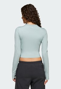 Jasnoniebieska, długorękawowa, krótka bluzka wykonana z gładkiej tkaniny, z zaokrąglonym dekoltem i dopasowanym krojem, zestawiona z ciemnymi, luźnymi spodniami.