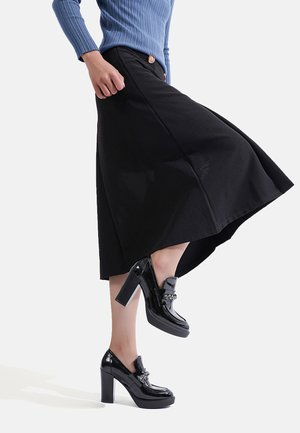 Gonna nera a campana in cotone con dettaglio a bottoni, abbinata a scarpe con tacco nere lucide con un accento decorativo a catena.