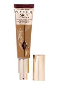 Tube du fond de teint Beautiful Skin de Charlotte avec distributeur pompe doré et bouchon assorti posé à côté sur fond blanc.