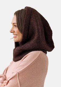 Dzianinowa kapturowa chusta w ciemno-brązowej wełnie, o luźnym, zwiewnym kroju. W połączeniu z miękkim różowym swetrem, który ma okrągły dekolt i prążkowaną fakturę.